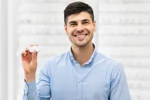 A man is holding a pair of glasses in his hand and smiling at the camera