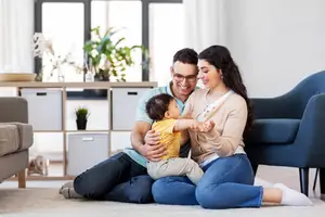 A family sitting on the floor with a baby, smiling and looking at the camera