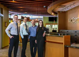 Four people in formal attire standing in front of a counter with a sign that reads McCormick Optometric