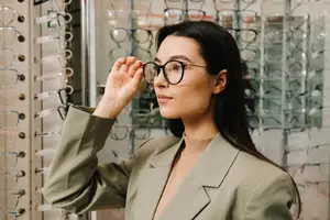 A woman tries on a pair of glasses at a store.
