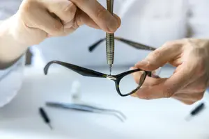 A person fixing eyeglasses with a screwdriver on a white table
