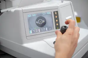 Close-up of an optometrist's hand adjusting a retinography machine with a monitor displaying a black circle and numbers.