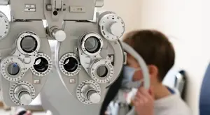 A young boy is examining his eyes with a slit lamp in a medical clinic.