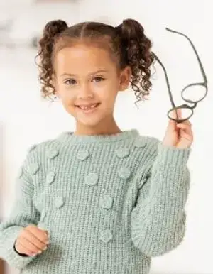 A smiling young girl holding a pair of glasses and wearing a green sweater with round dots