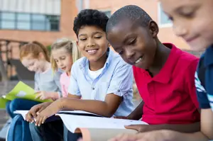 A group of young kids sitting on a bench and smiling while looking at books.