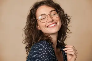 Woman with curly hair wearing glasses and a polka-dot shirt smiling and posing for a photo