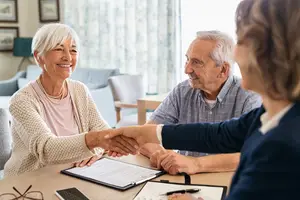A woman shakes hands with a man and a woman in a living room