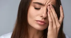 Close up of a woman with her eyes closed and her head tilted to the side holding her forehead with her hand