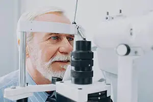 An elderly man with white hair and a beard is having his eyes examined with a medical device.