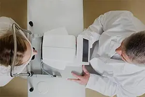 A woman and a man in white coats are examining an eye with a medical device.