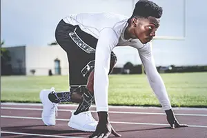 A man in a white long-sleeve shirt and black shorts is getting ready to run on a track.