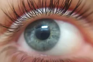 A close-up of a human eye with long, curled eyelashes and a slightly open eyelid, focusing on the iris and pupil with a soft focus effect.