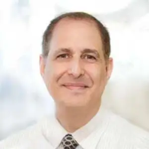 A man wearing a white shirt and tie is smiling for a photograph