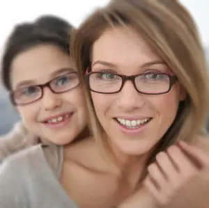A woman and a young girl both wearing glasses and smiling at the camera