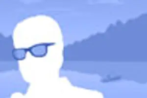 A silhouette of a person with sunglasses standing by the water with a boat in the background