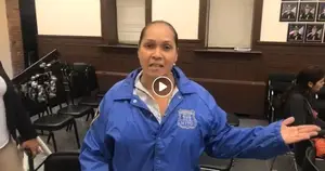 A woman wearing a blue NYPD jacket is standing in a room with chairs and a podium