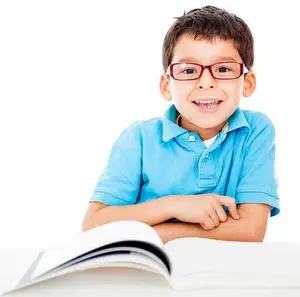 A boy in a blue polo shirt with eyeglasses is smiling and posing for a photo while sitting at a table with an open book in front of him.