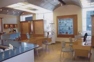 A blurry image of an interior space that is possibly an office or a store with a tiled floor, glass windows, wooden tables, and chairs, and a glass display case with items inside.