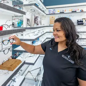A woman in a black shirt is looking at glasses in an optical shop.