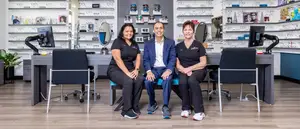 Three people sitting on a bench in front of a desk in an office.