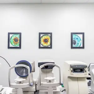 Three frames with colorful images of eyes are mounted on the wall above three machines, possibly used for eye examinations, in a room.