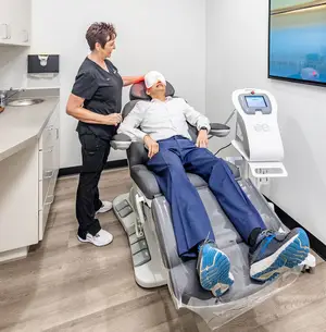 An older man wearing a blindfold is getting his eyes treated by a woman in a clinic room