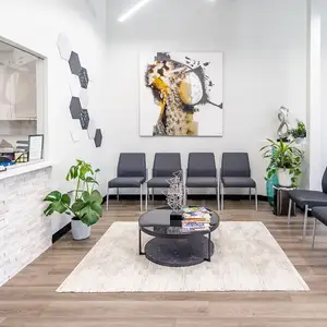 A modern living room with a large white rug, a round table, and a large painting on the wall.