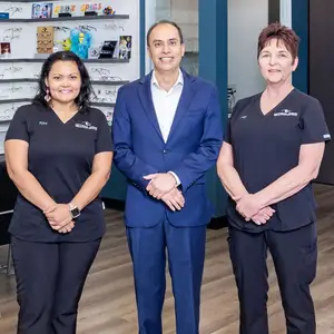 Three employees standing together in front of shelves of glasses at an optical shop