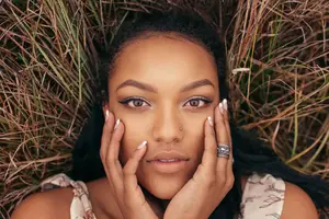 A woman lying on dried grass with her hands on her cheeks