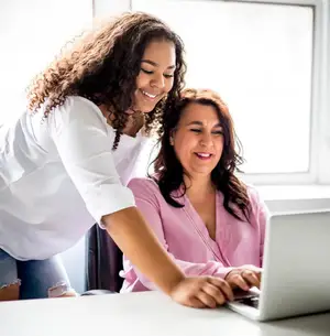 Two smiling women looking at a laptop screen in an office setting