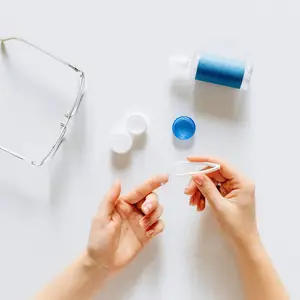 A person wearing a ring is using a pair of tweezers to remove a contact lens from a contact lens bottle.