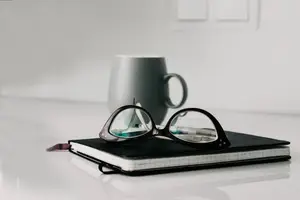Black glasses and a coffee cup on top of a notebook on a white table