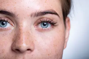 Close-up of a woman's face with blue eyes and freckles on her cheeks.