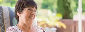 Elderly woman wearing glasses smiling at camera while sitting on chair on porch