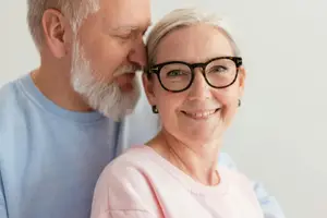 An elderly couple is smiling and posing for a photo with a white background.
