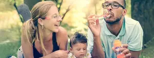 A man, woman, and child are blowing bubbles in a park.