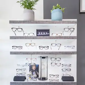 A shelf displays a variety of DKNY eyeglasses, accompanied by potted plants, a picture frame, and an hourglass on a white background.
