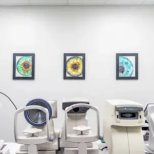 A room with three framed paintings above machines that look like they belong to an eye clinic.