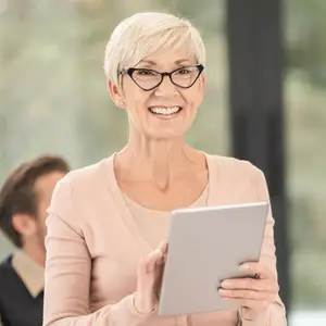 A woman is holding a tablet and smiling while standing in front of a man in an indoor area.
