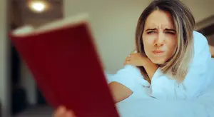 woman in bed with book reading and having bad reaction