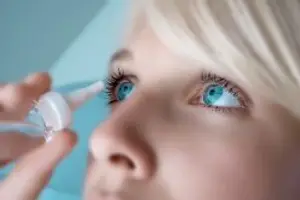 A woman with blue eyes is using eye drops to treat her dry eyes.