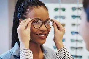 A woman in a denim jacket is trying on glasses in front of a rack of sunglasses