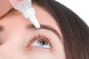 Close up of a woman applying eye drops to her eye.