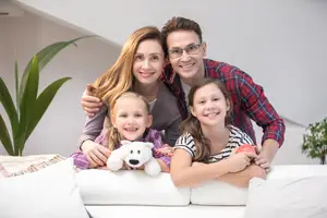 Four people are smiling while sitting on a couch in a room with white walls.