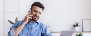 A smiling man talking on his phone while sitting at his desk in an office