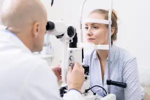 A woman with a bun hairstyle getting her eyes checked by a male doctor using an ophthalmoscope