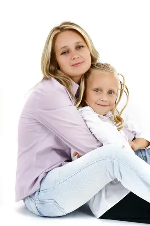 A woman with blonde hair is sitting on the floor with a smiling girl in a white shirt.