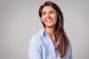 Portrait of a smiling woman with brown hair wearing a blue striped shirt