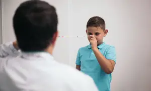 A boy is blowing his nose while a doctor looks at him in a hospital room