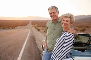 Senior couple smiling on the side of the road with their car